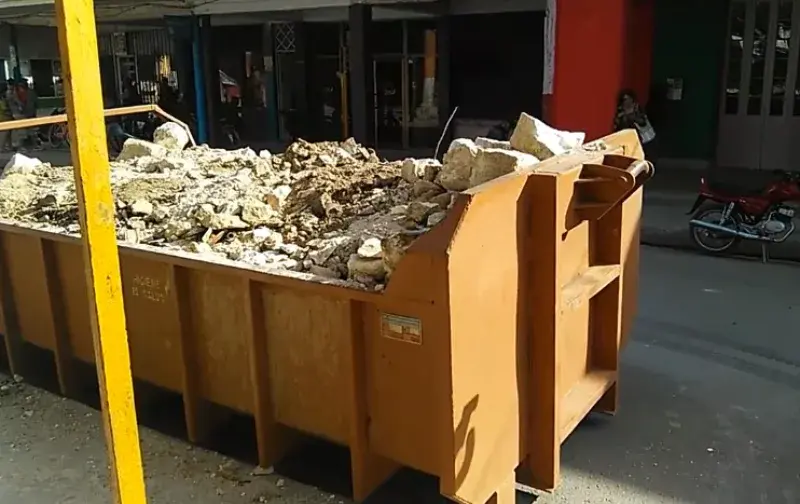 Heavy demolition debris including lumber and drywall in a dumpster